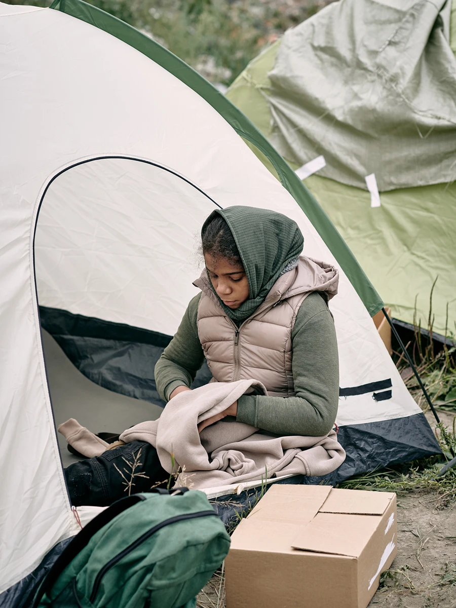 Girl sitting outside a tent, holding clothes.